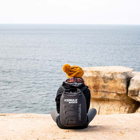 A hiker wears her IceMule cooler overlooking the ocean from a beachside cliff.